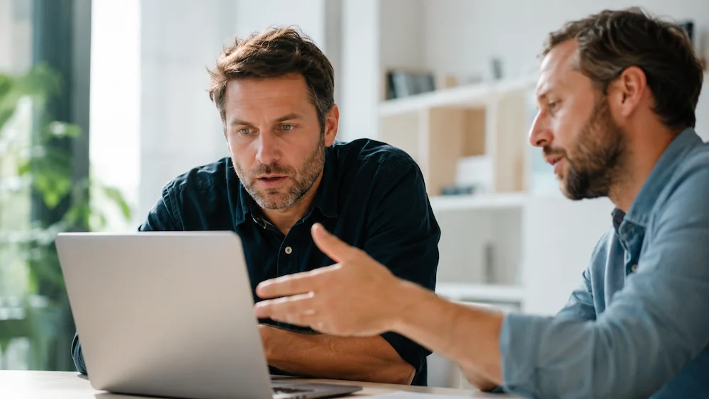 Un dirigeant captivé découvre la première impression de son site web sur un ordinateur portable, sa webdesigner à ses côtés